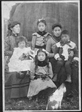 Black and white image of woman sitting with adopted Japanese daughter and surrounded by other children